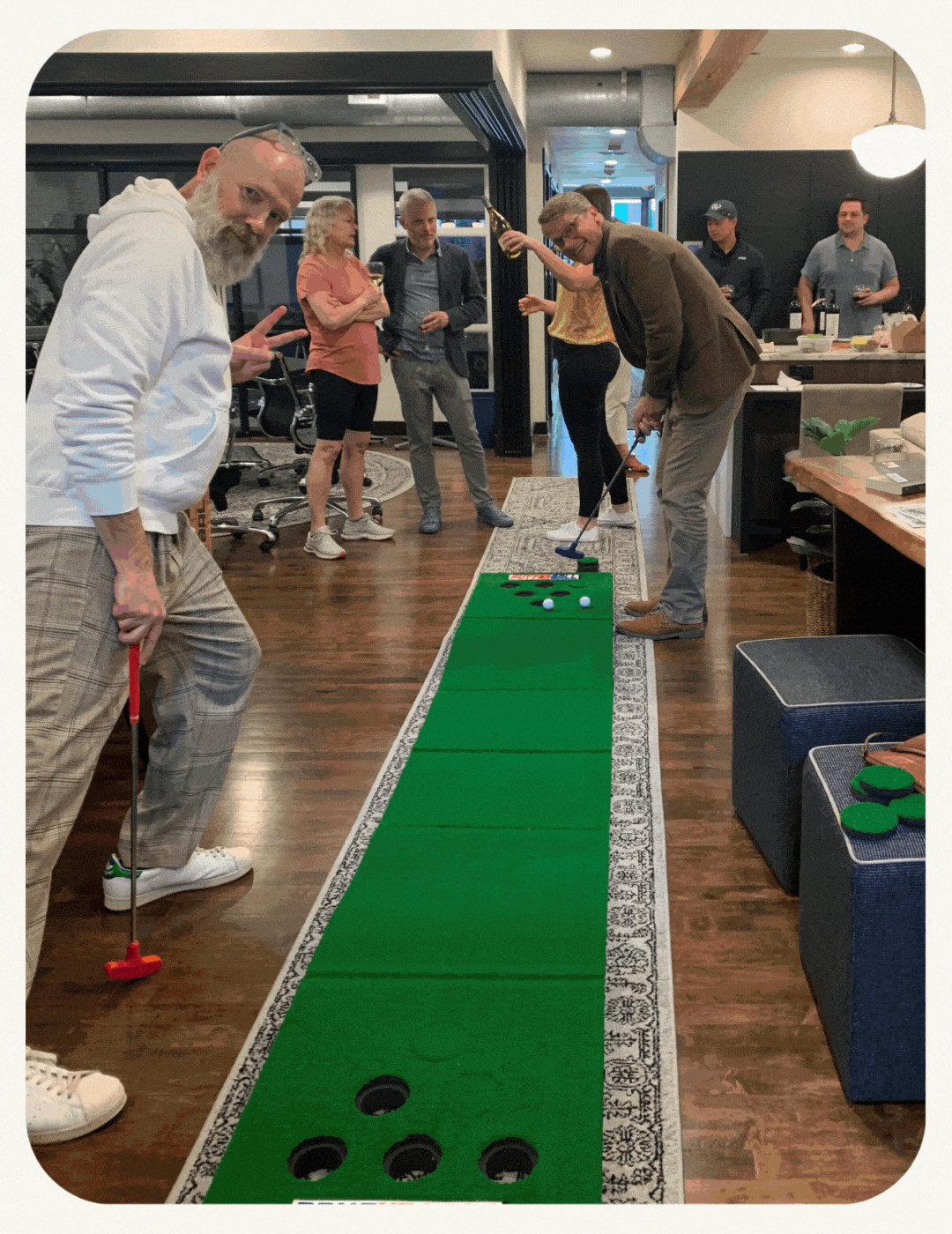 A group of adults playing an indoor putting green game during a social gathering in a modern office space.