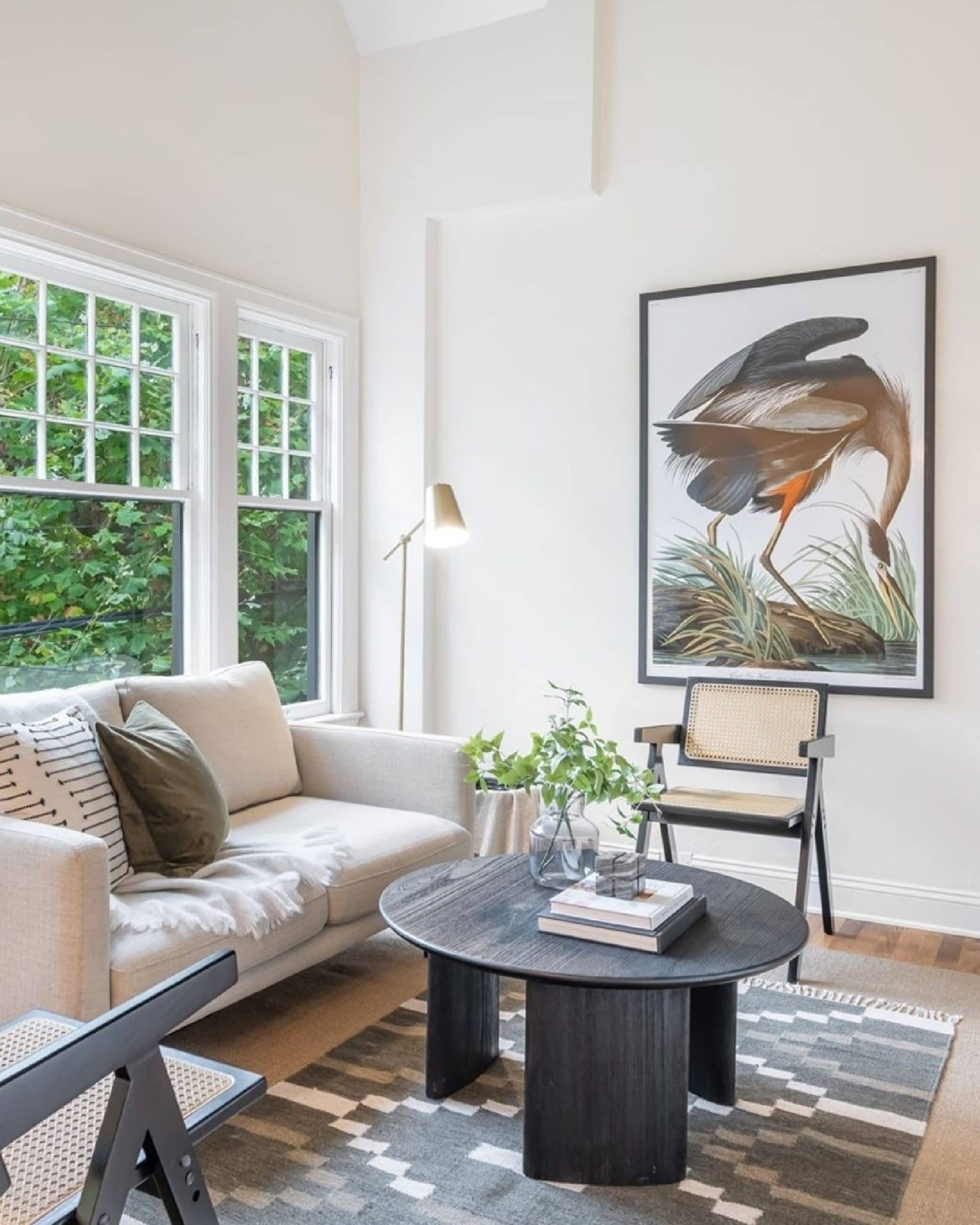 Modern living room featuring a cream sofa, black round coffee table, and large framed heron artwork on a white wall.