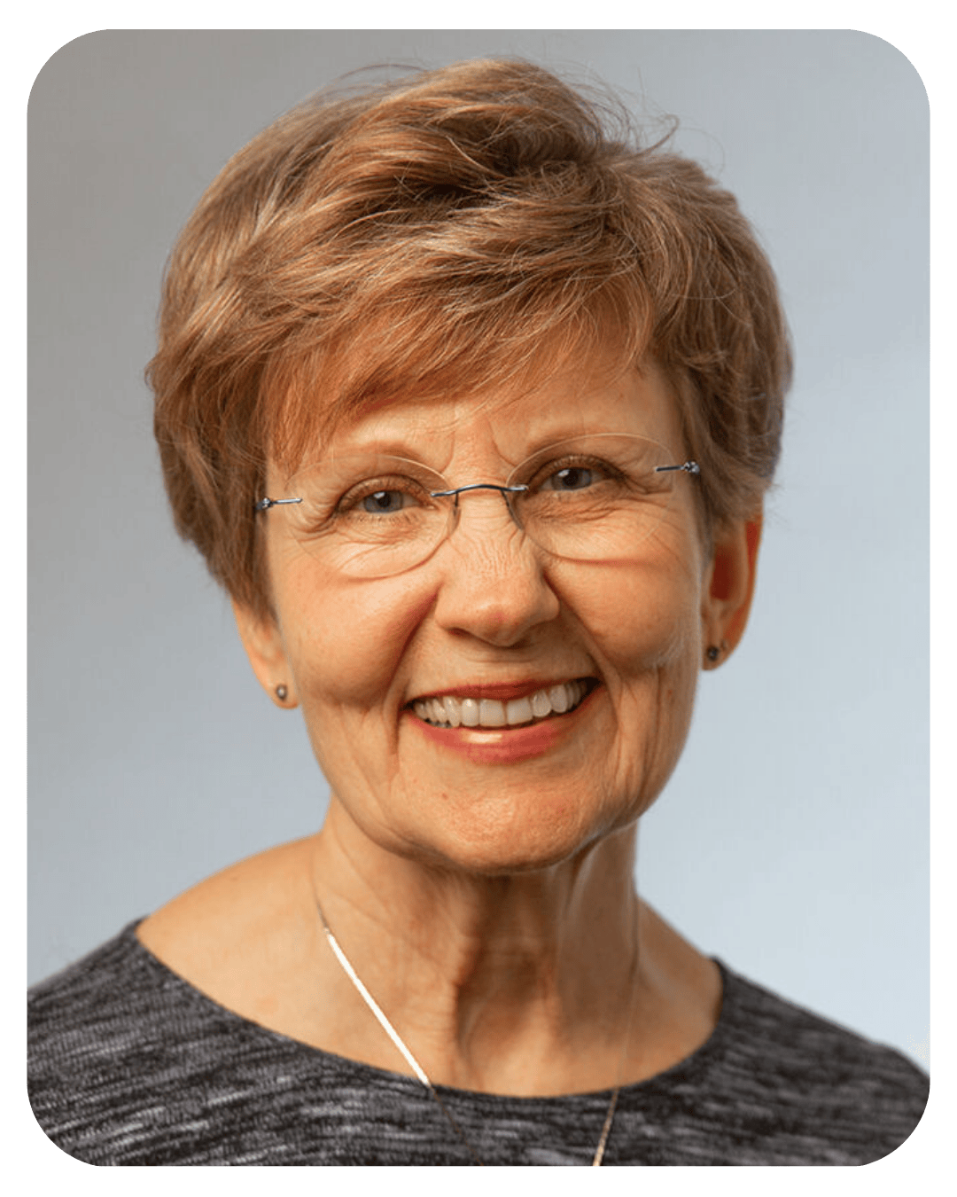 Smiling older woman with short reddish-brown hair and rimless glasses in a professional headshot.