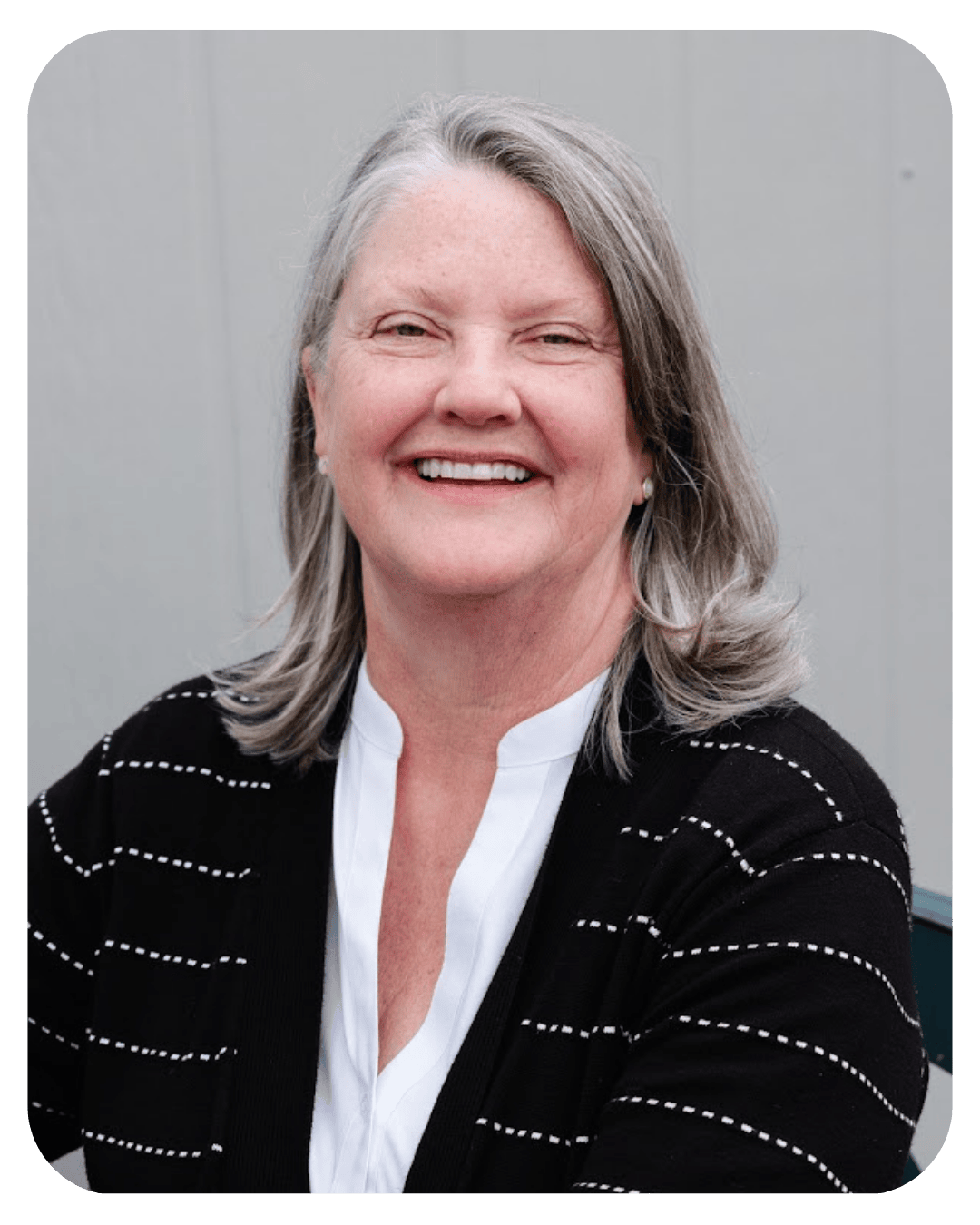 Smiling woman with grey hair wearing a black and white cardigan and white blouse.
