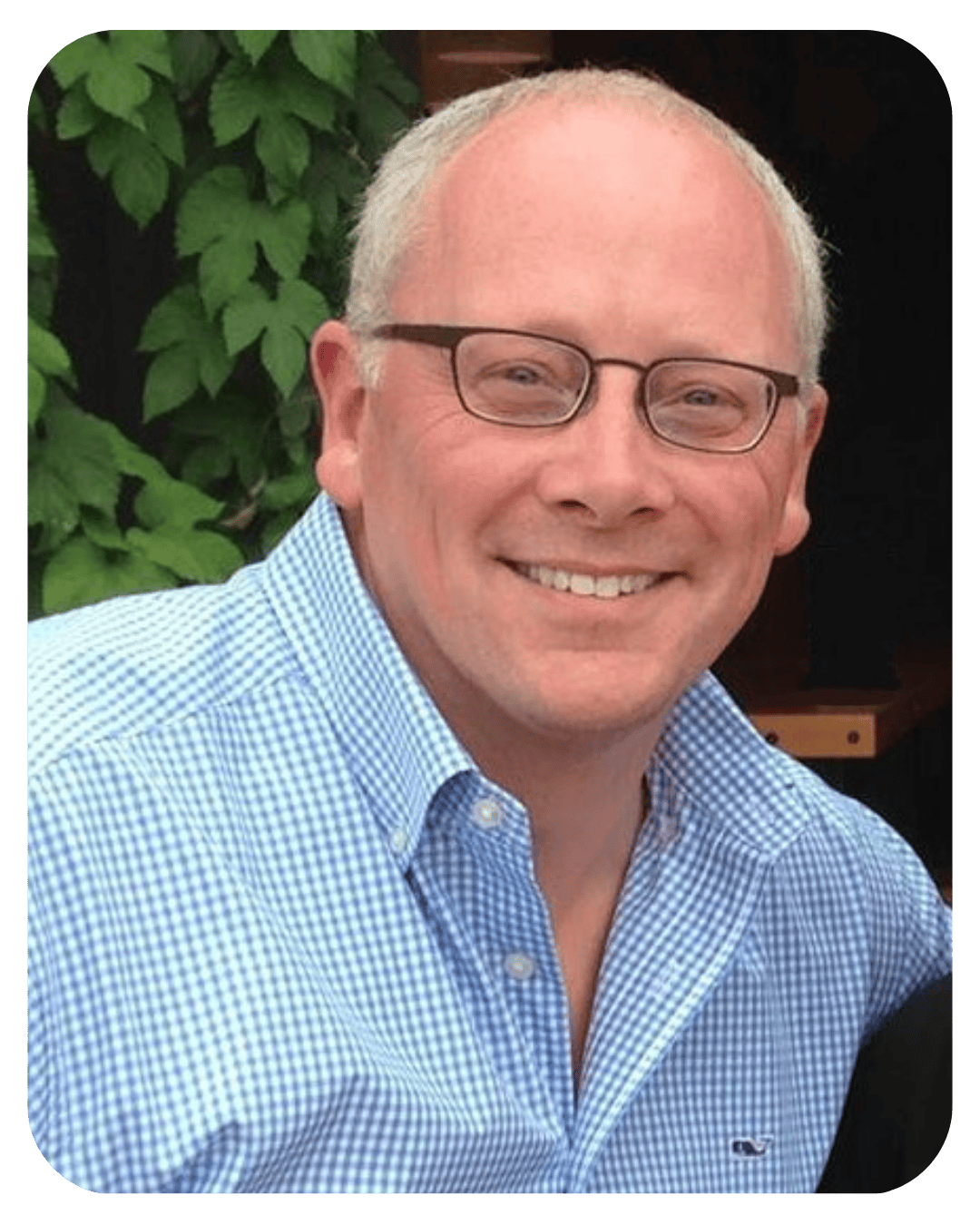 Smiling middle-aged man with short grey hair wearing glasses and a blue and white checkered button-down shirt.