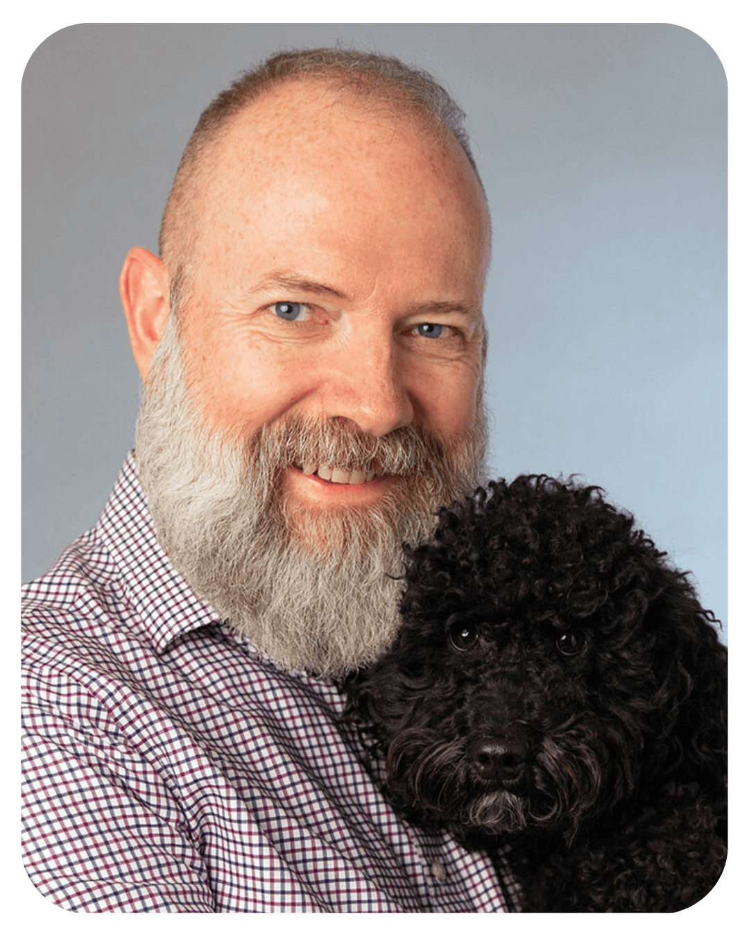 Smiling middle-aged man with a full grey beard holding a small black curly-haired poodle.