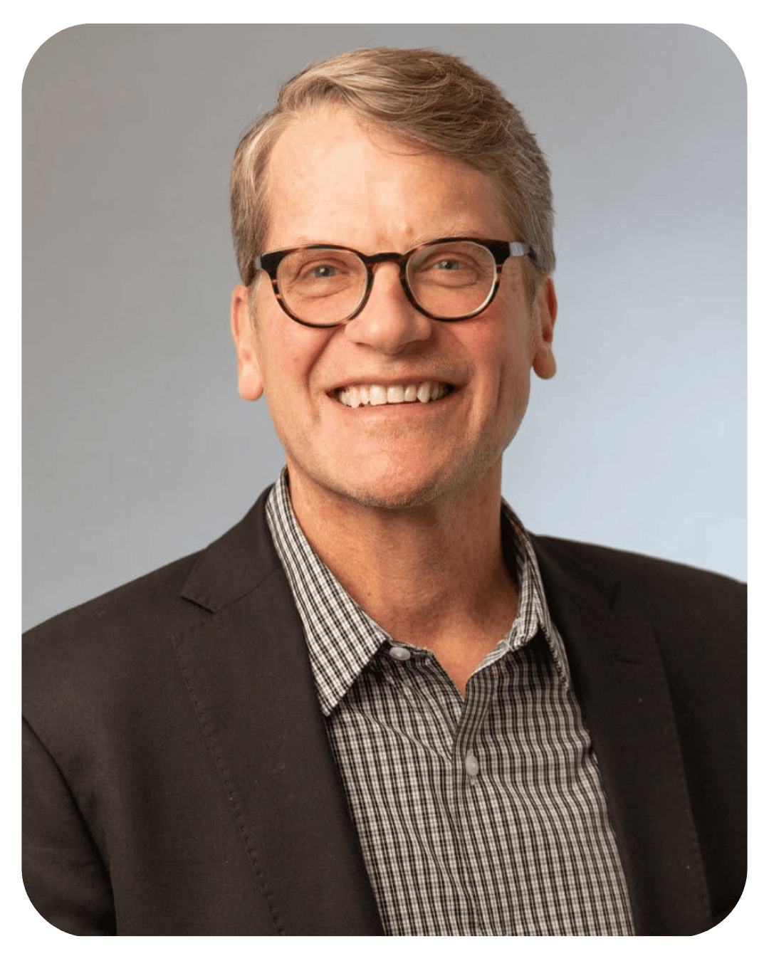 Professional headshot of a smiling middle-aged man with glasses wearing a dark blazer and checkered shirt.