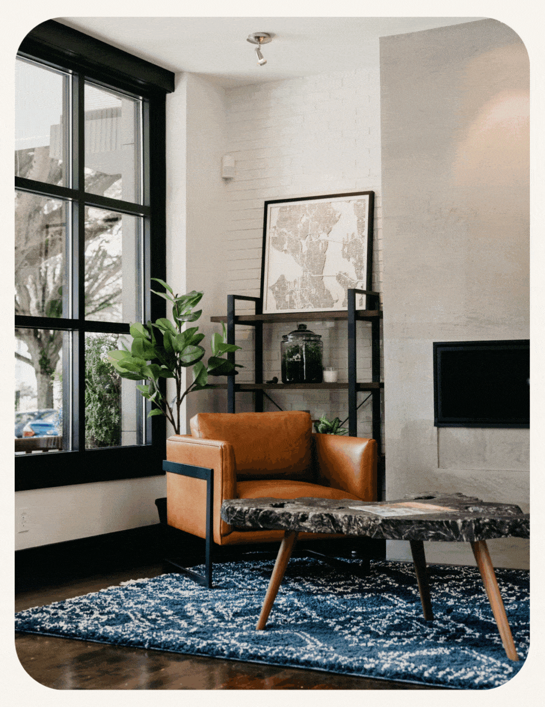 Tan leather armchair and stone coffee table on a blue rug in a modern living room with a large window.